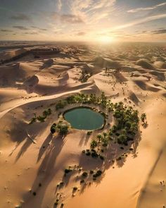 an aerial view of the desert with a small lake surrounded by sand dunes and palm trees