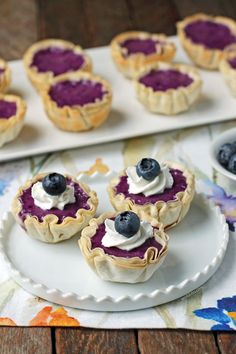 mini blueberry pies with whipped cream on a white plate next to other small desserts