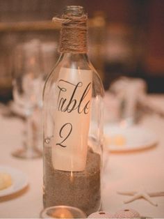 a bottle filled with sand sitting on top of a table next to glasses and plates