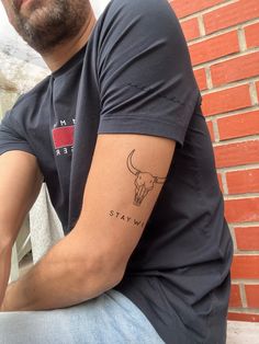 a man with a tattoo on his arm sitting next to a brick wall and window