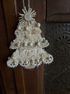 a white christmas tree ornament hanging from a wooden door with beads and pearls