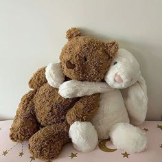 two brown and white teddy bears hugging each other on a pink surface with gold stars