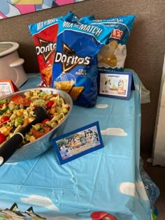 a table topped with lots of food next to a bag of chips and a bowl of salad