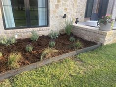 a garden bed in front of a house with plants growing out of the ground next to it