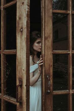 a woman in a white dress is looking out the window