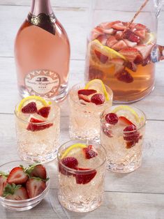 several glasses filled with ice and strawberries next to a bottle