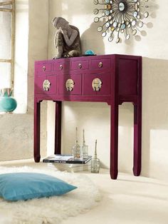 a pink table with two drawers and a blue pillow on it in front of a window