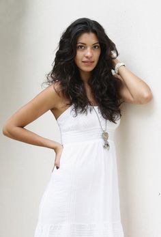 a woman in a white dress leaning against a wall with her hand on her head