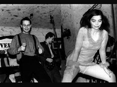 black and white photograph of people playing music in a room with guitar, bass, and microphone