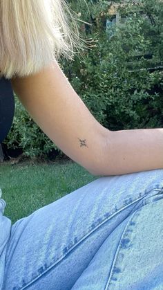 a woman with a small star tattoo on her left arm sitting in front of some bushes