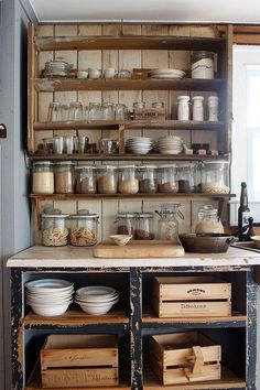 an old fashioned kitchen with lots of dishes on the shelves and wooden crates in front of it