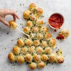 a christmas tree made out of rolls with sauce on the side and hands holding a spoon