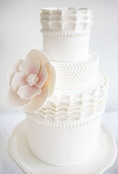 a three tiered cake with white frosting and flowers on the top, sitting on a plate