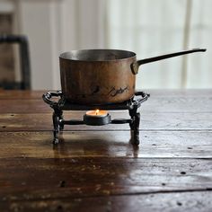 an old cast iron pot sitting on top of a wooden table next to a candle