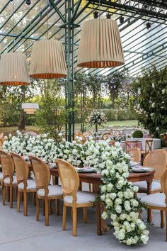 an outdoor dining area with wooden chairs and tables covered in white flowers, surrounded by greenery