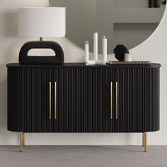 a black and gold sideboard next to a white lamp with a round mirror on the wall