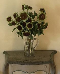 a vase filled with lots of sunflowers on top of a wooden table next to a wall