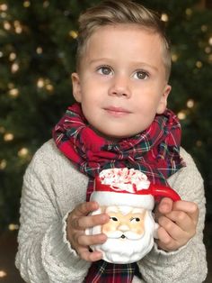 a little boy holding a cup with santa clause on it and wearing a scarf around his neck