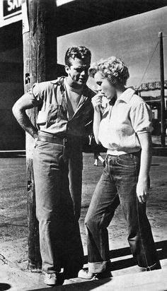 an old black and white photo of two people standing next to each other on the street