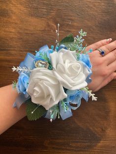 a bridal bouquet with white roses and blue flowers on the bride's wrist