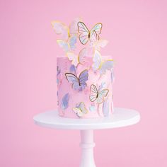 a pink cake with butterflies on it sitting on a white pedestal against a pink background