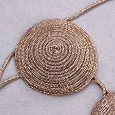 a gold necklace with circles and tassels hanging from it's side on a gray surface