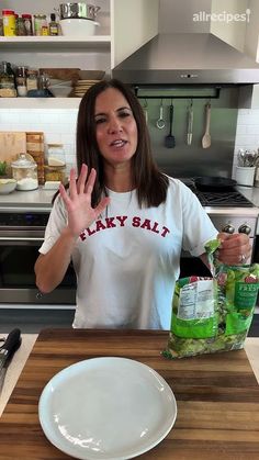 a woman standing in front of a wooden table holding up her hands and making the peace sign