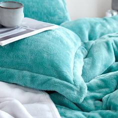 a coffee cup sitting on top of a bed next to a book and pillow cover