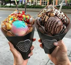 two people holding up ice cream cones with different toppings on them in front of a city street