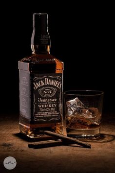 a bottle of jack daniels whiskey next to a glass with an ice cube in it