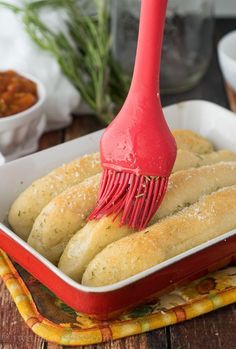 a red spatula being used to brush bread in a casserole dish on a wooden table