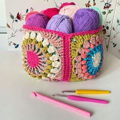 a crochet basket filled with balls of yarn next to two crocheted knitting needles