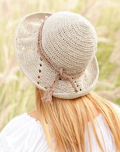 a woman wearing a crocheted hat in the middle of a grassy area with tall grass