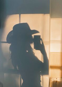 the shadow of a woman wearing a hat holding a camera in front of a window