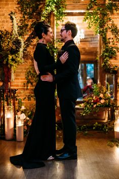 Bride in a black wedding dress hugs her groom in his black suit. They are standing in front of their dark and moody Halloween wedding ceremony altar with climbing florals and glowing candles. Naturalist Aesthetic, Victorian Naturalist, Carondelet House Wedding, Chargers Plates, Carondelet House, Halloween Wedding Dresses, Dinner Party Wedding, House In Los Angeles, Aesthetic Dinner