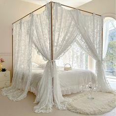 a white bed sitting in a bedroom next to a window with sheer curtains on it