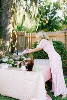 a woman in a pink dress standing over a table