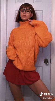 a woman in an orange sweater and red skirt poses for the camera with her hands on her hips