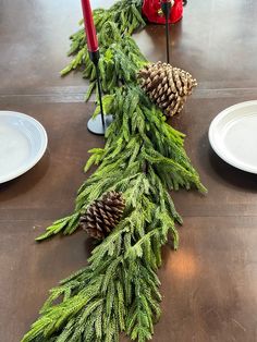 a table with pine cones and evergreen branches on it, along with two red candles