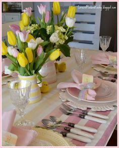 the table is set with pink and yellow flowers in vases, silverware, and plates