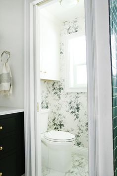 a white toilet sitting in a bathroom next to a green tiled wallpapered wall