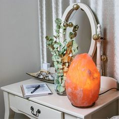 an orange vase sitting on top of a white table next to a mirror and plant