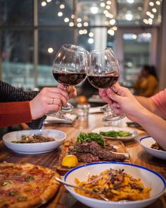 two people toasting wine glasses over a table full of food