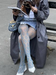 a woman sitting on a park bench reading a magazine wearing tights and high heels