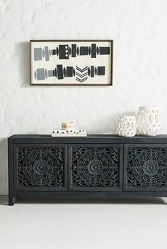 a black cabinet with two vases on top of it and a framed picture above it