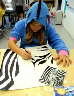 a girl in a blue hoodie is painting zebras on a piece of paper