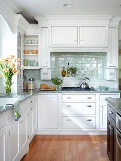 a kitchen with white cabinets and wood floors is pictured in this image, there are flowers on the counter