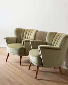 two green chairs sitting next to each other on top of a hard wood floor in front of a white wall