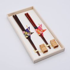 two chopsticks in a wooden box on a white surface with an origami decoration