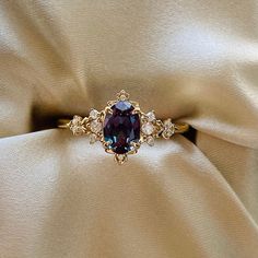 a ring with an oval shaped purple stone surrounded by smaller round diamonds on top of a beige fabric